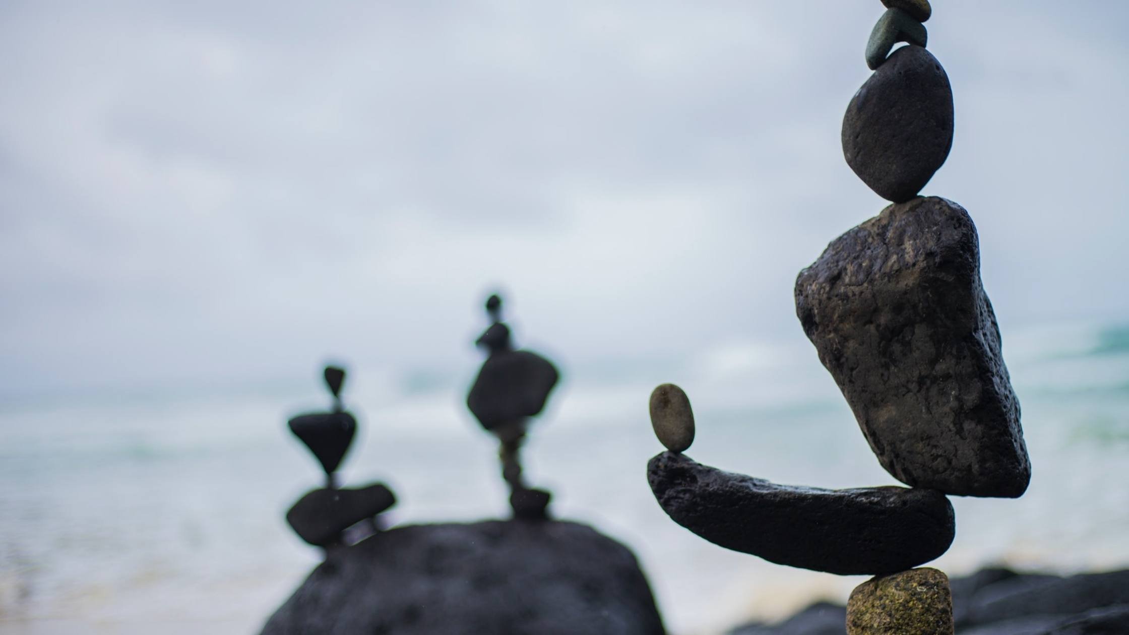 Three sets of stacked stones, balanced on rocks near the ocean