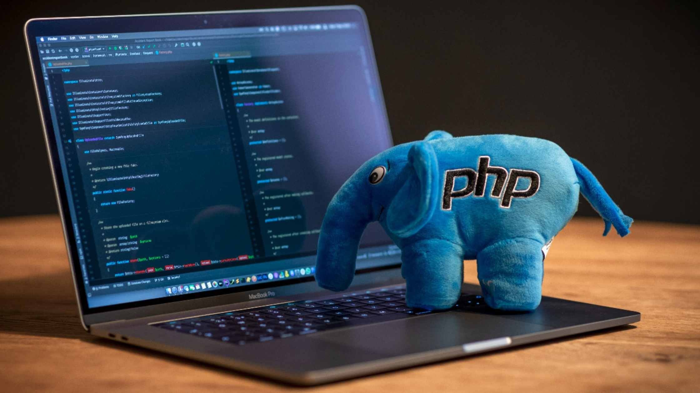 PHP programming concept; Blue plush elephant with embroidered PHP logo standing on laptop