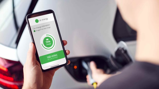 Person charging electric vehicle while looking at charging app on mobile phone