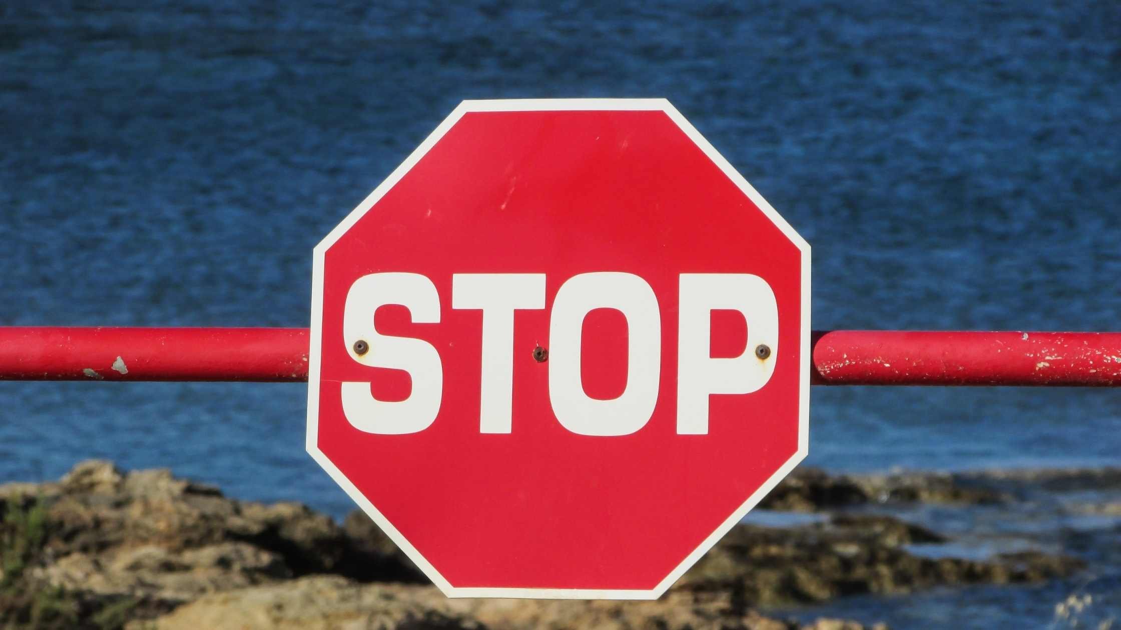 Red stop sign attached to a barrier, sea and sky in the background