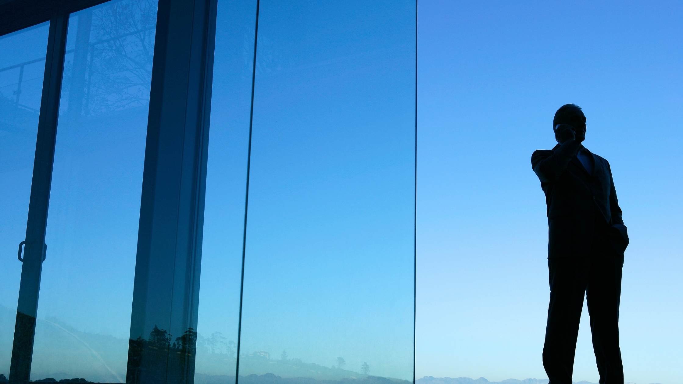 Silhouette of man talking on mobile phone in front of glass house