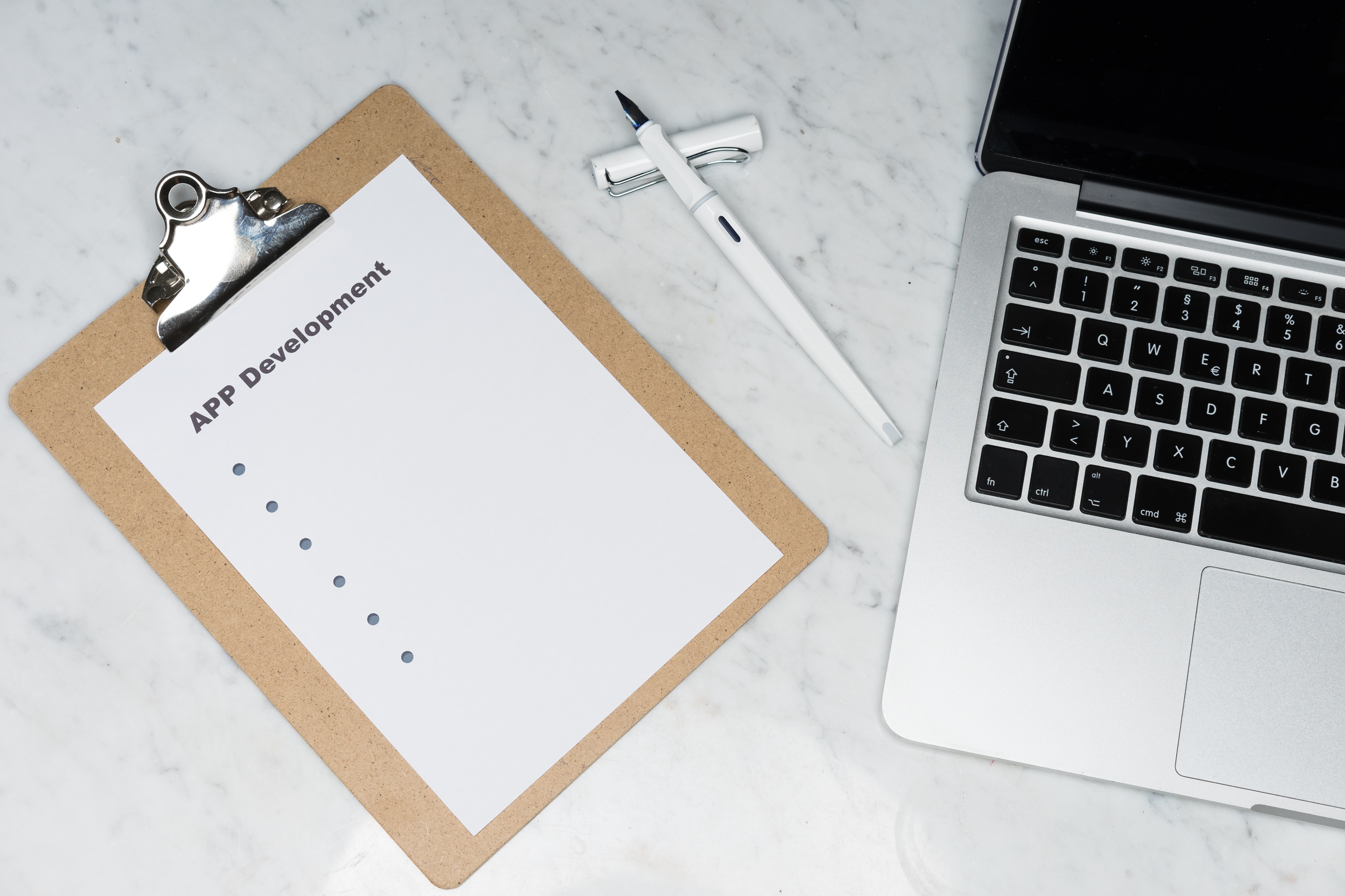 Laptop in a desk with a paper todo list for app development on its left side