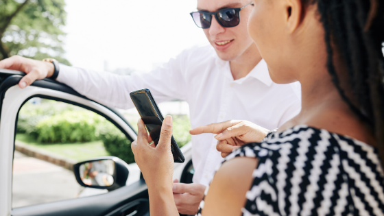 Woman pointing to mobile phone talking to a man standing next to car