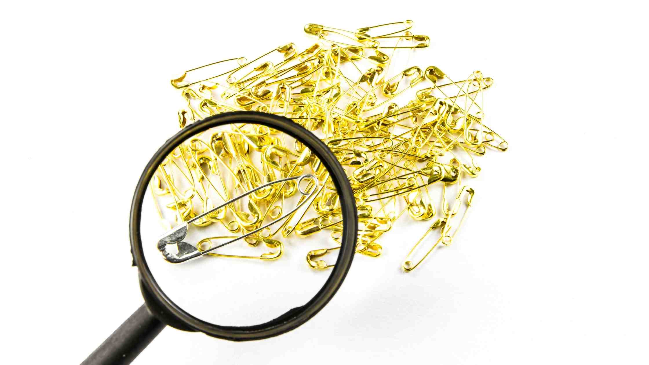 Safety pins and magnifying glass on a white background